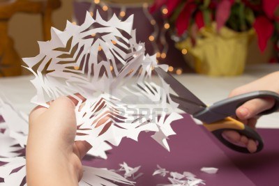 Person cutting out a paper snowflake with scissors