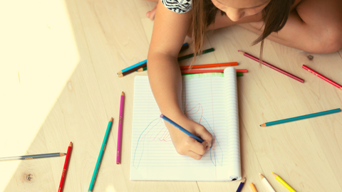 A child drawing a picture on a in a notebook with colored pencils